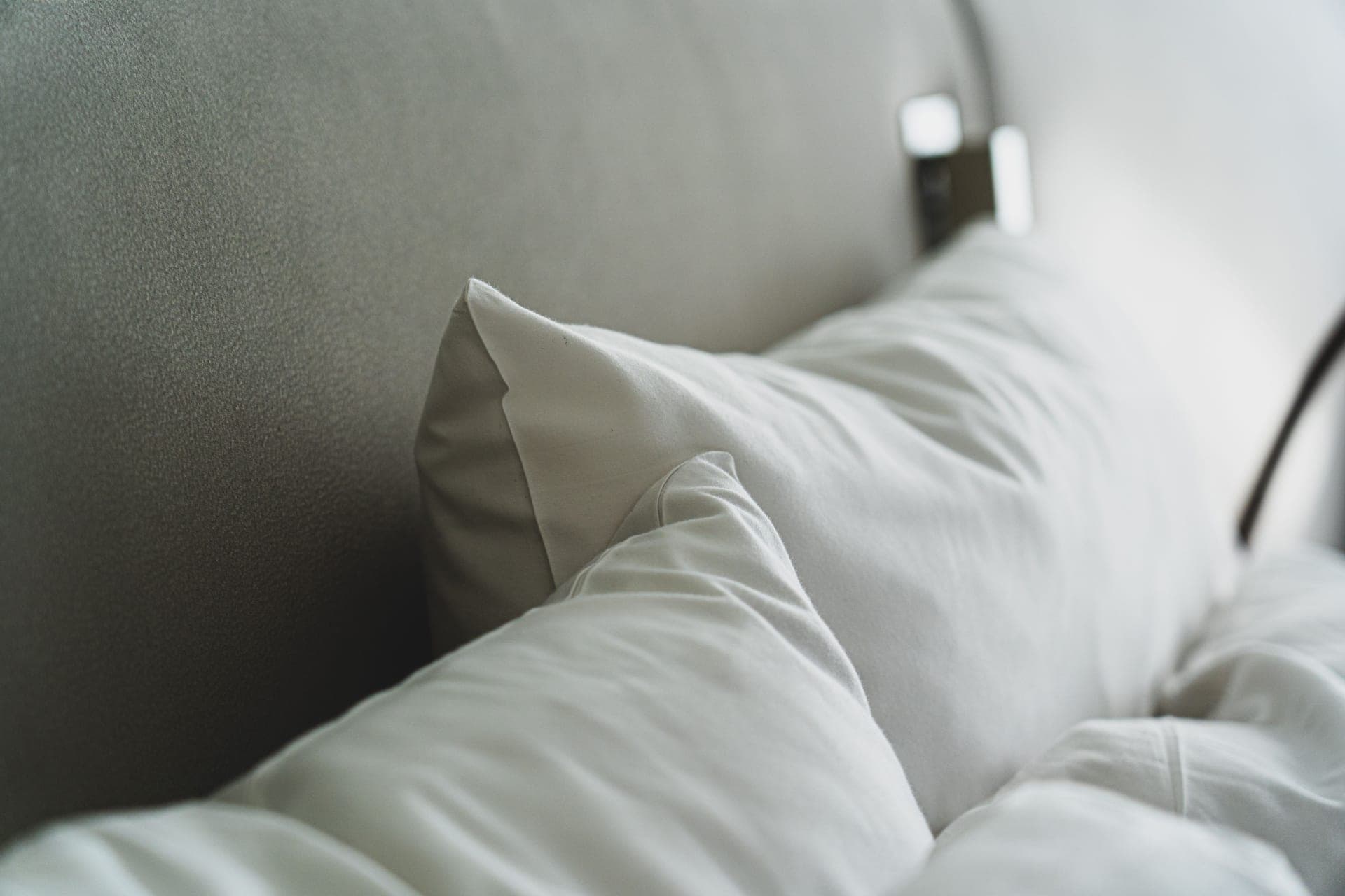 Plump pillows stacked against a linen headboard in soft daylight